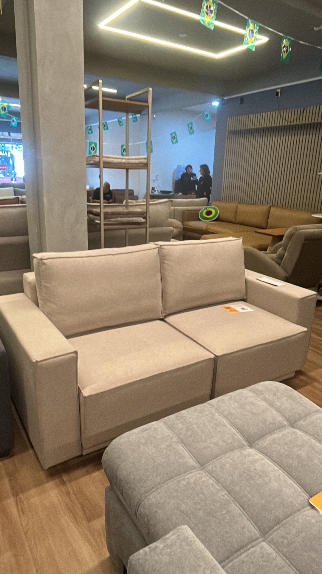 Sofá retrátil bege de 2 lugares com puff cinza acolchoado ao lado no showroom da Art's Colchões, Ingleses Florianópolis