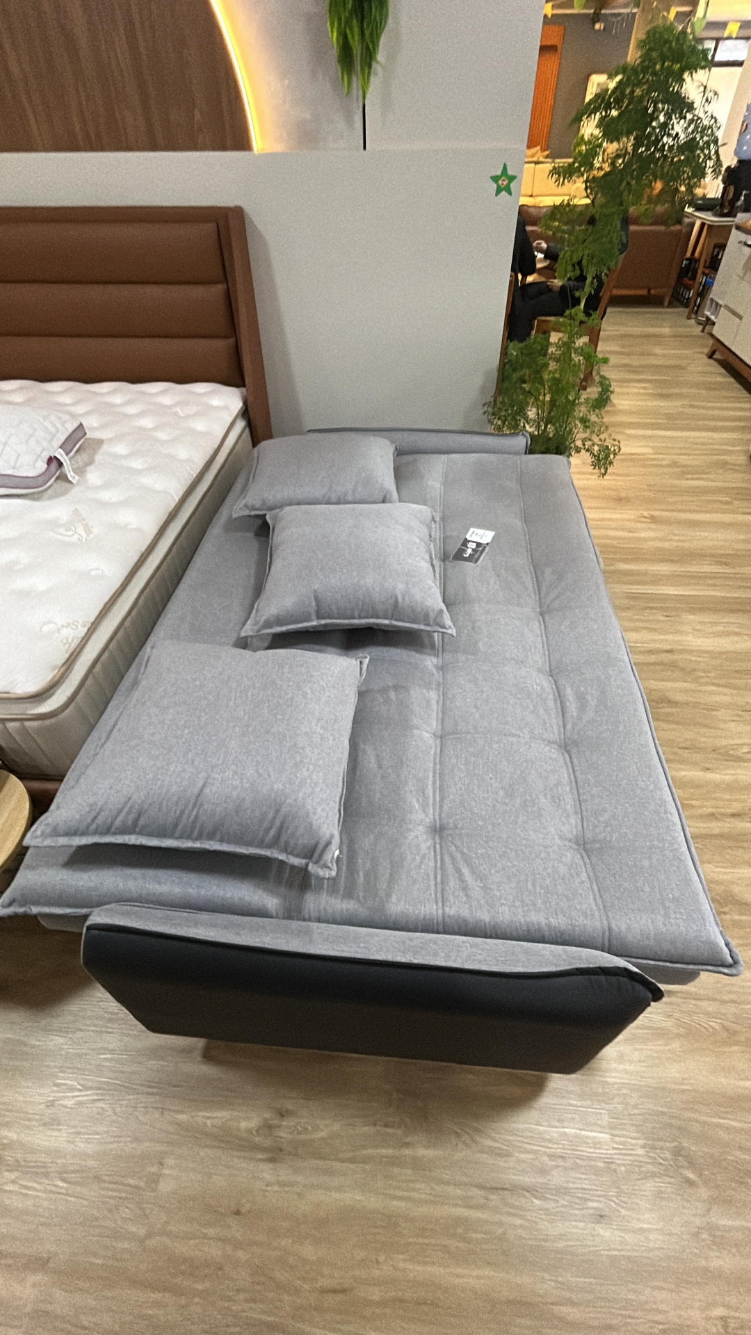 Sofá-cama aberto em posição de dormir com almofadas cinza sobre o colchão no showroom da Art's Colchões, Ingleses Florianópolis
